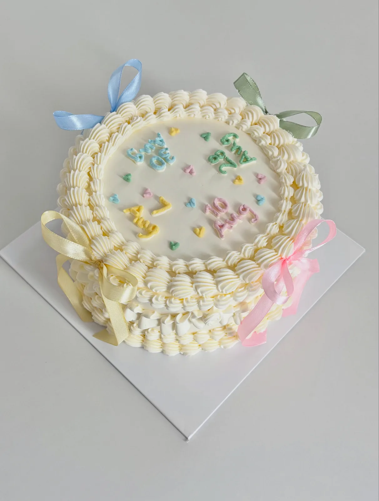 Cream cake with pastel confetti piping and blue bow, custom cake made in Streatham SW16 - Danine Cakes