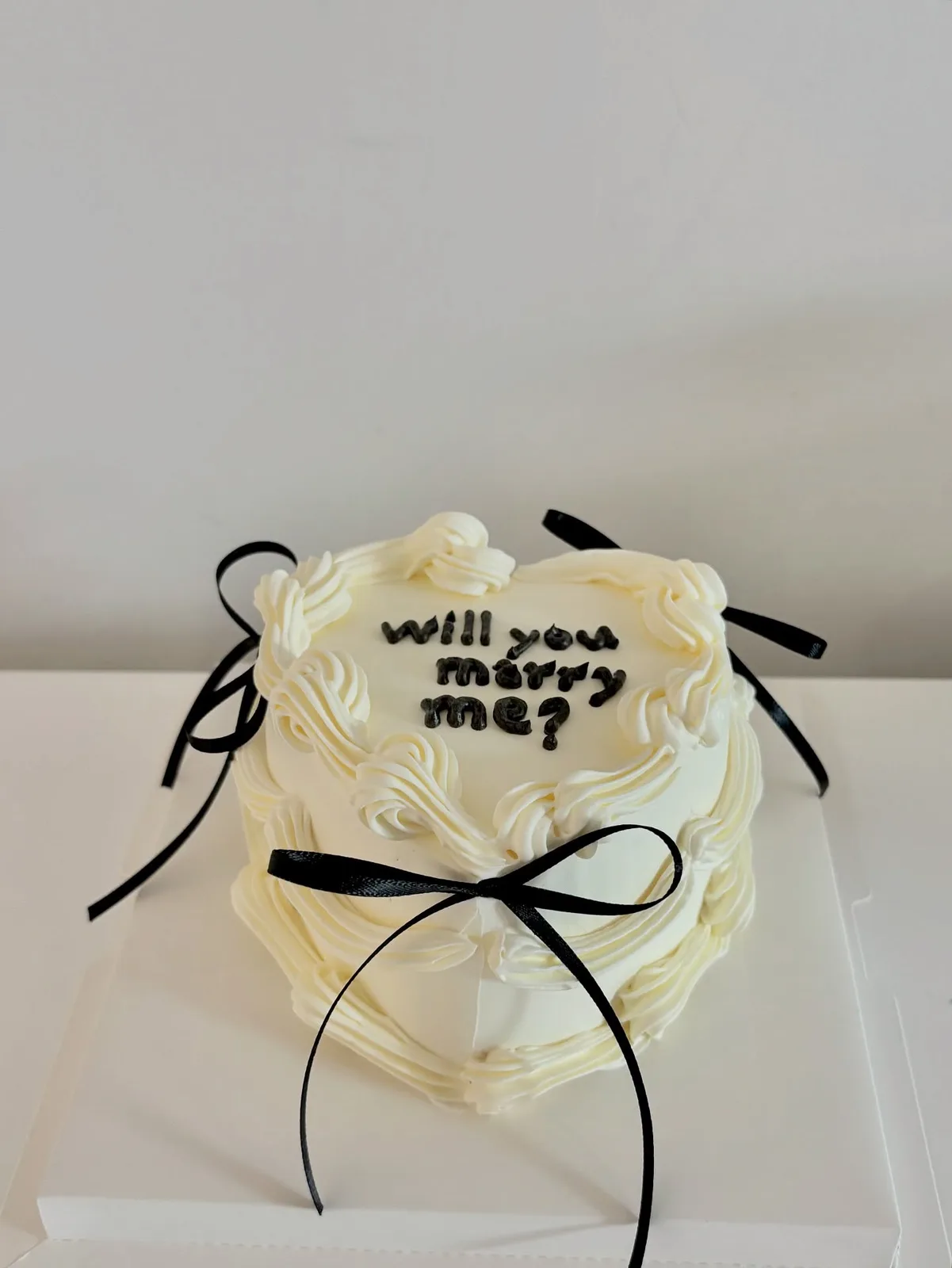 Ivory cake with black bows and piped proposal lettering, bespoke celebration cake from Danine Cakes, South London