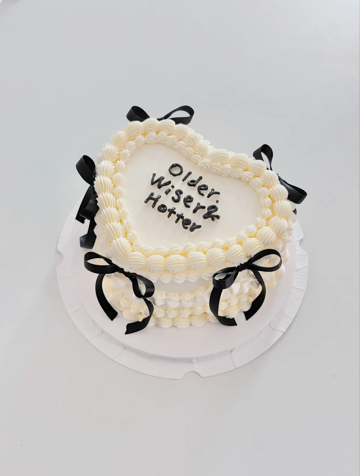 Ivory heart cake with black bows and piped lettering, handmade to order by Danine Cakes in Streatham, South London