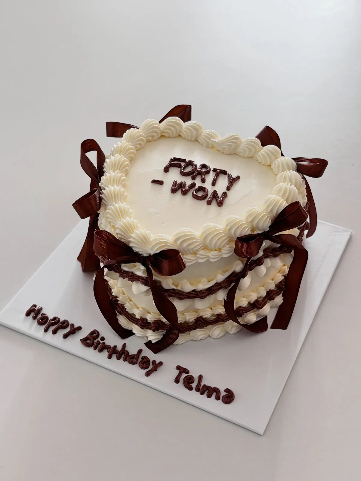 Ivory heart cake with brown bows and piped lettering, bespoke celebration cake from Danine Cakes, South London