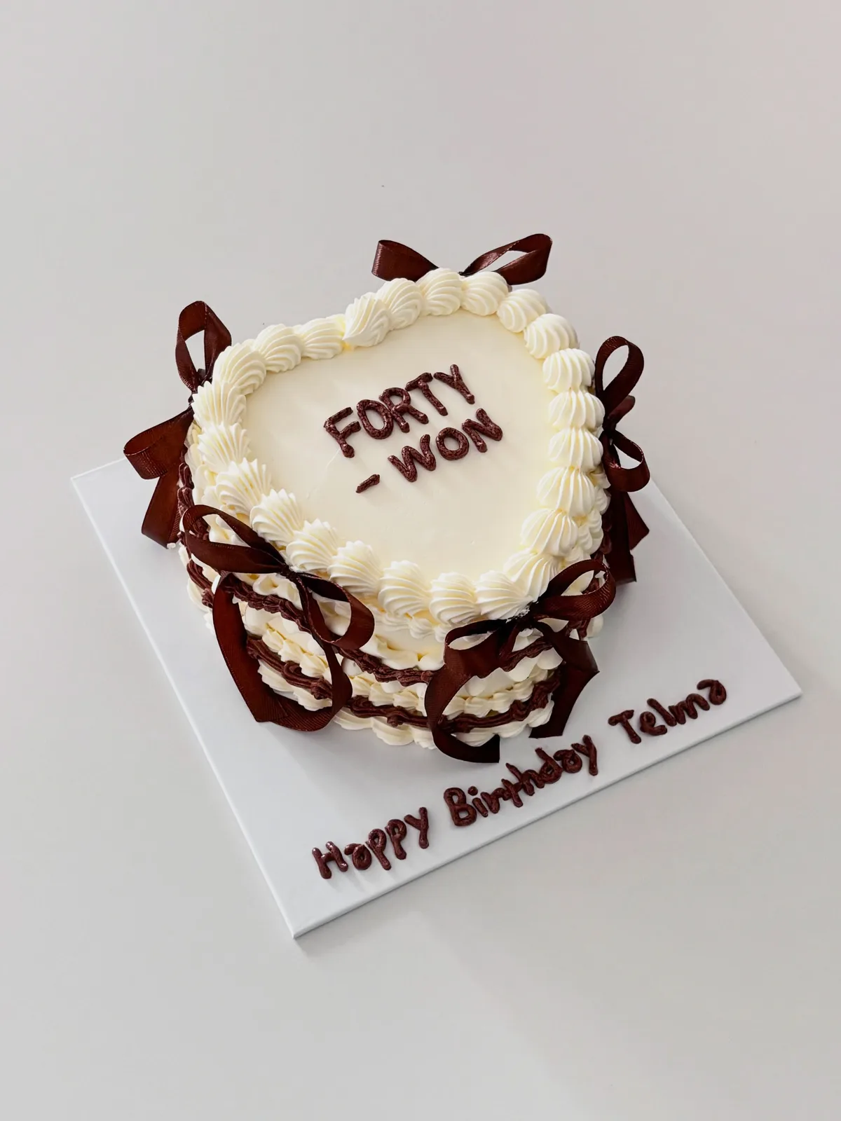 Ivory heart cake with brown bows and piped lettering, bespoke celebration cake from Danine Cakes, South London