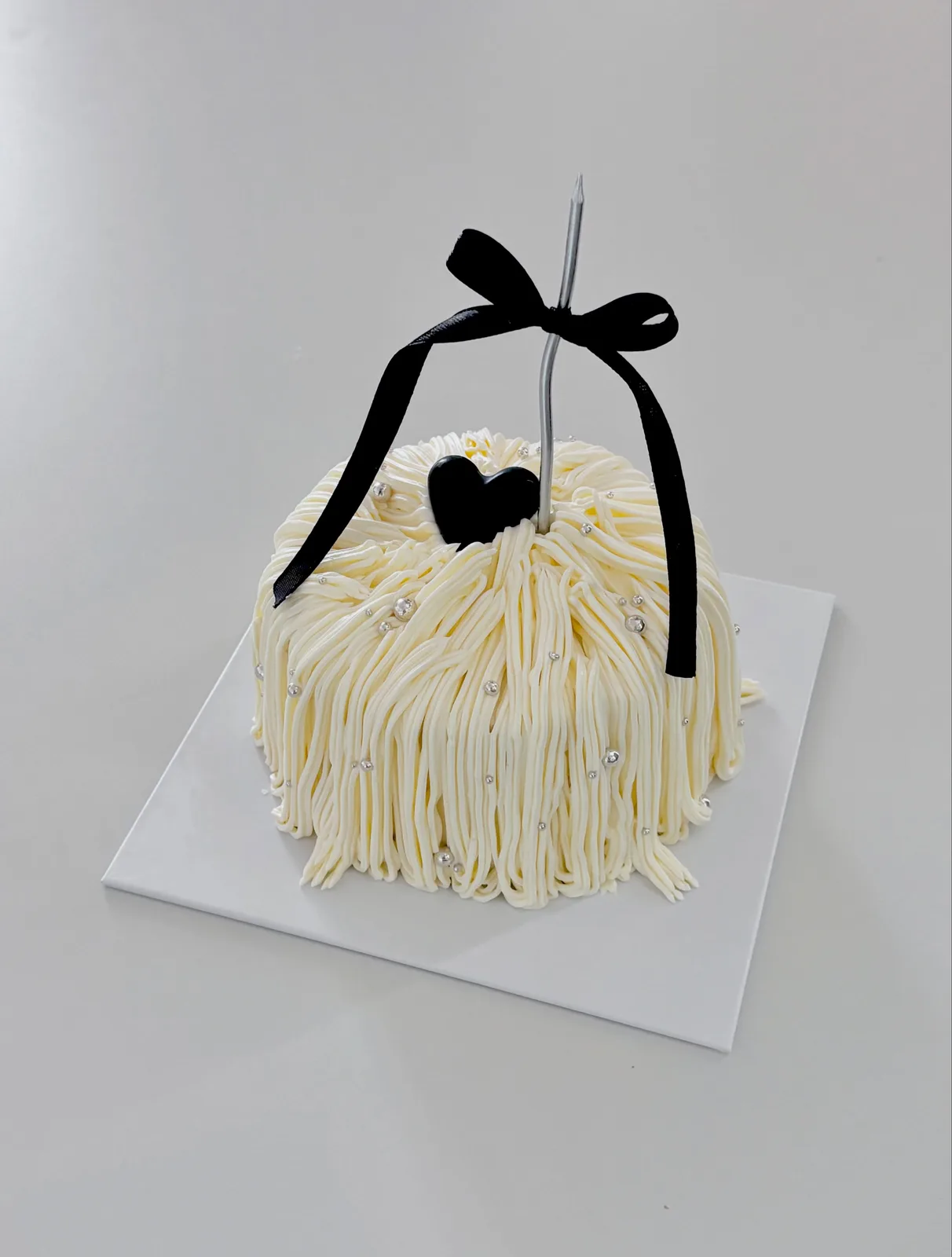 Ivory piped strand cake with black bow and heart, handmade to order by Danine Cakes in Streatham, South London