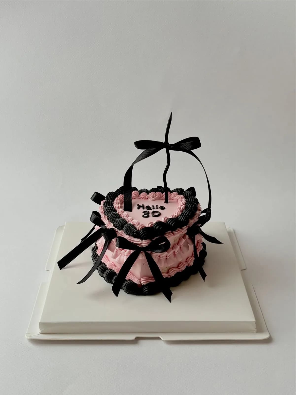 Pink cake with black lace piping and bow, bespoke celebration cake from Danine Cakes, South London