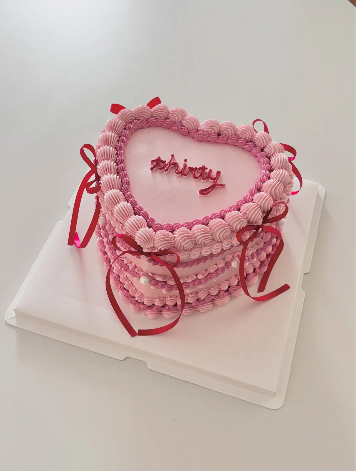 Pink heart cake with red ribbons and piped border, handmade to order by Danine Cakes in Streatham, South London