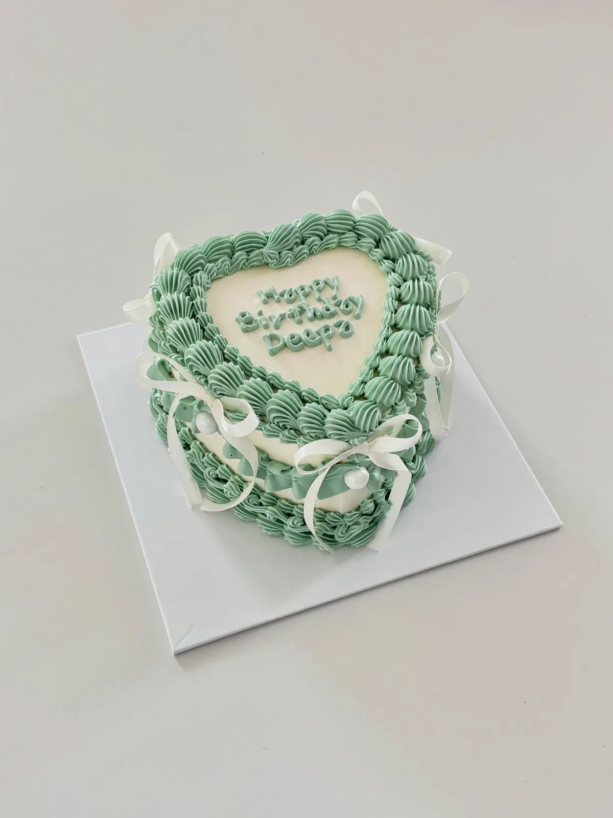 Sage green heart cake with white bows, Korean-inspired custom cake handmade in Streatham, London