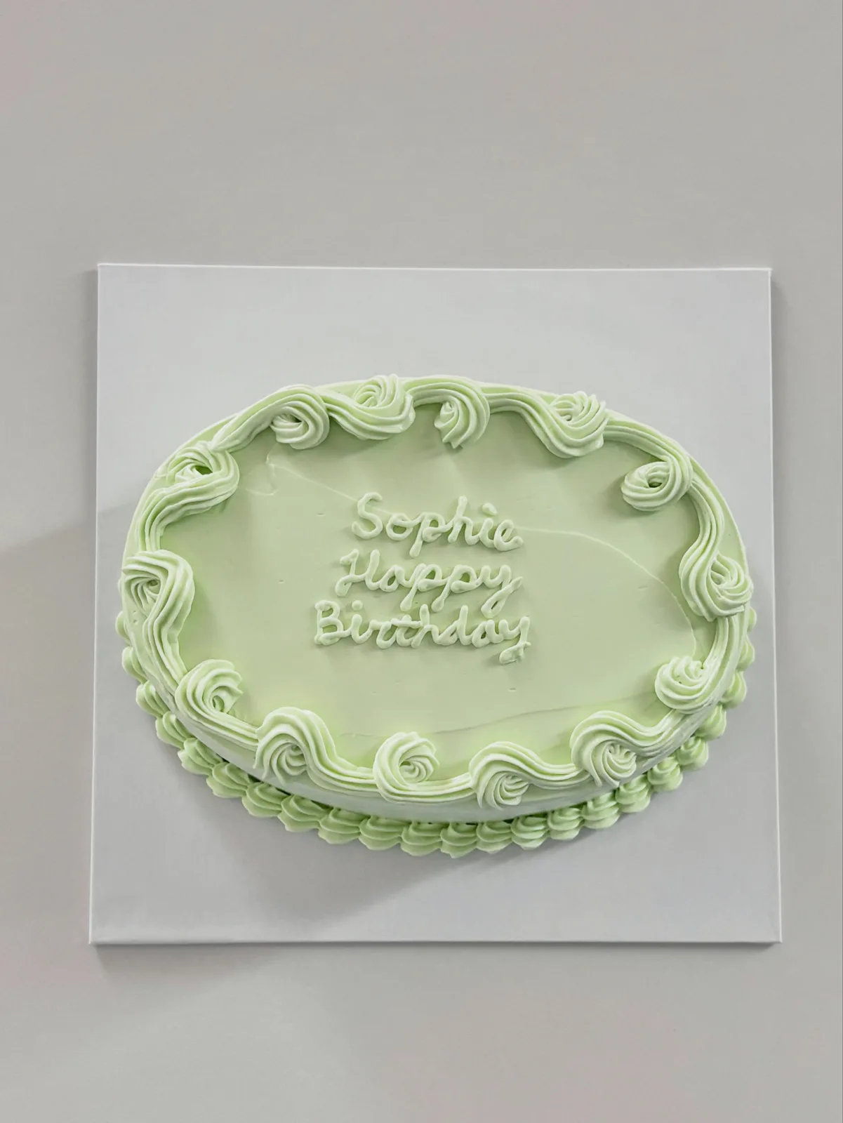 Sage green oval cake with piped scroll border, bespoke celebration cake from Danine Cakes, South London