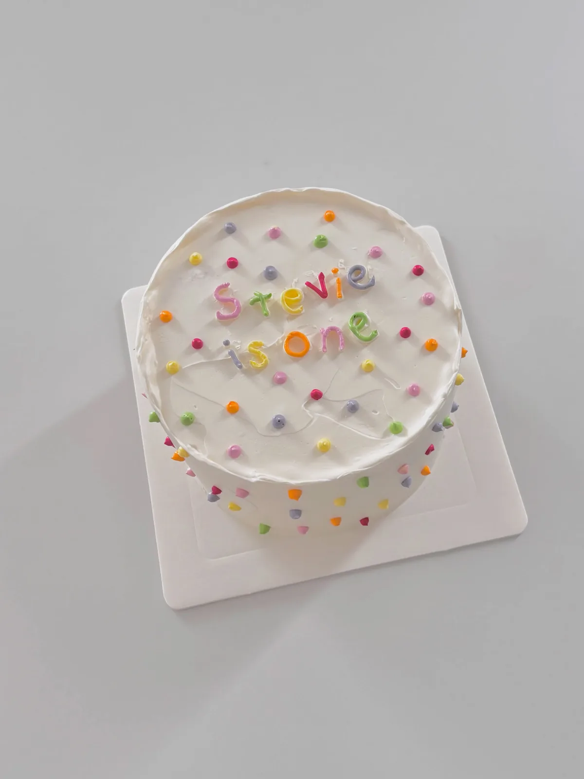 White cake with rainbow confetti dots and lettering, handmade to order by Danine Cakes in Streatham, South London