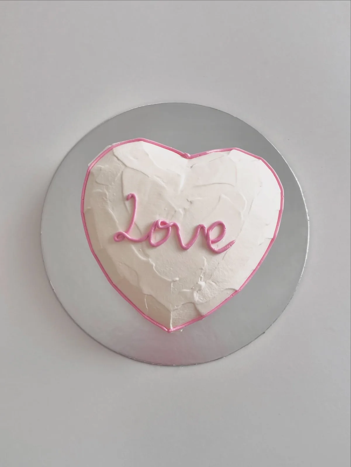 White heart cake with pink piped Love lettering, bespoke celebration cake from Danine Cakes, South London