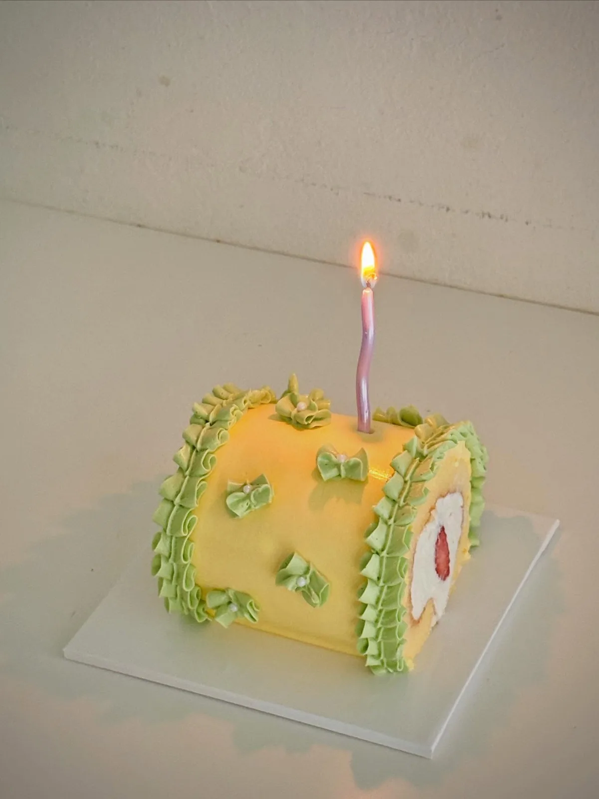 Yellow swiss roll cake with green bows and candle, Korean-inspired custom cake handmade in Streatham, London
