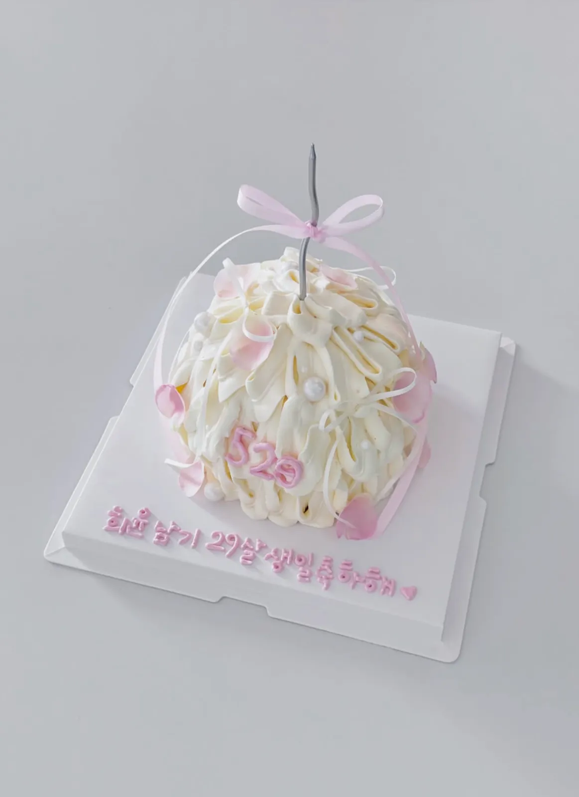 White piped buttercream dome cake with a pink ribbon bow and rose petals
