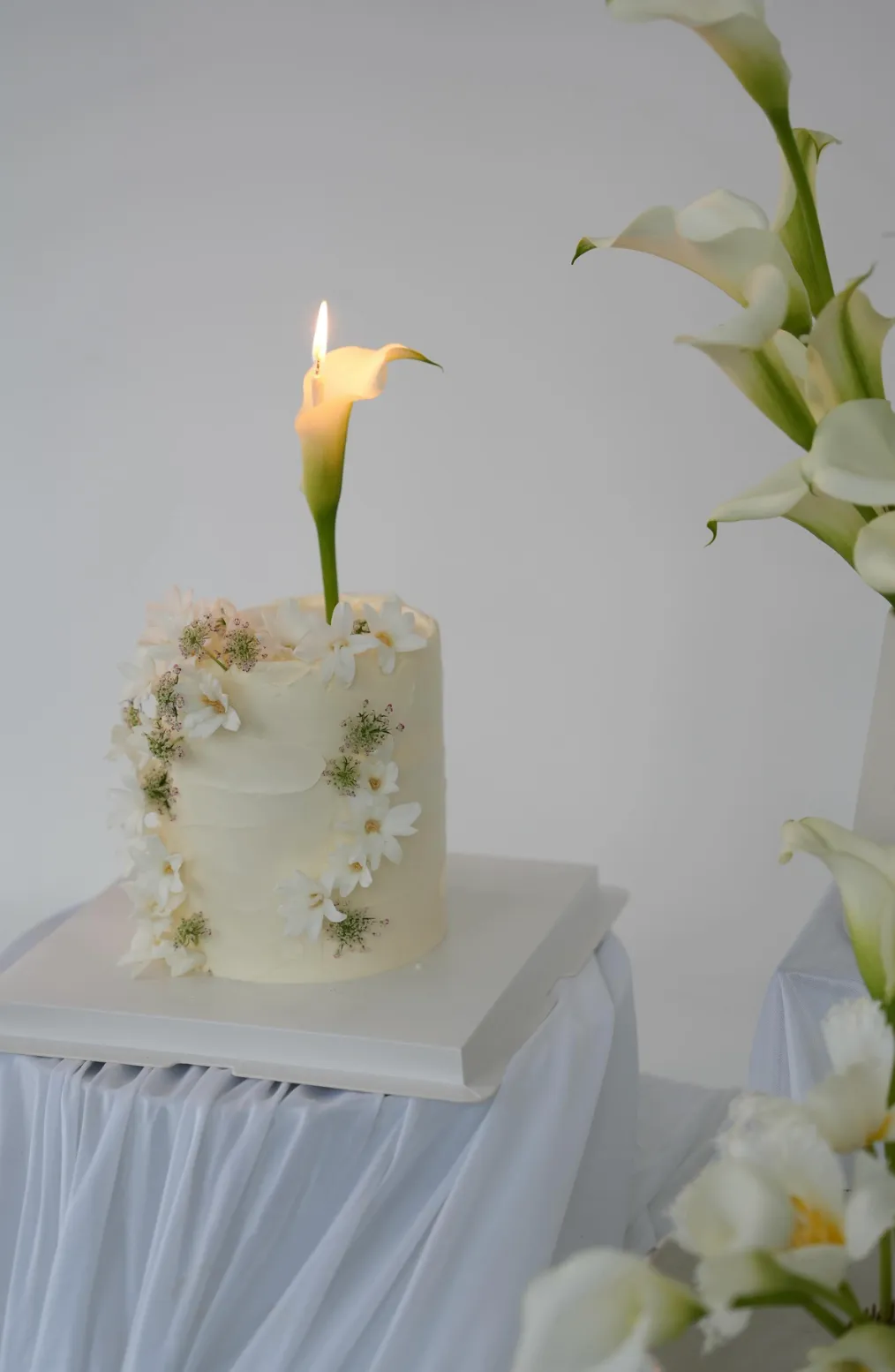 White celebration cake with fresh white daisies and a calla lily candle