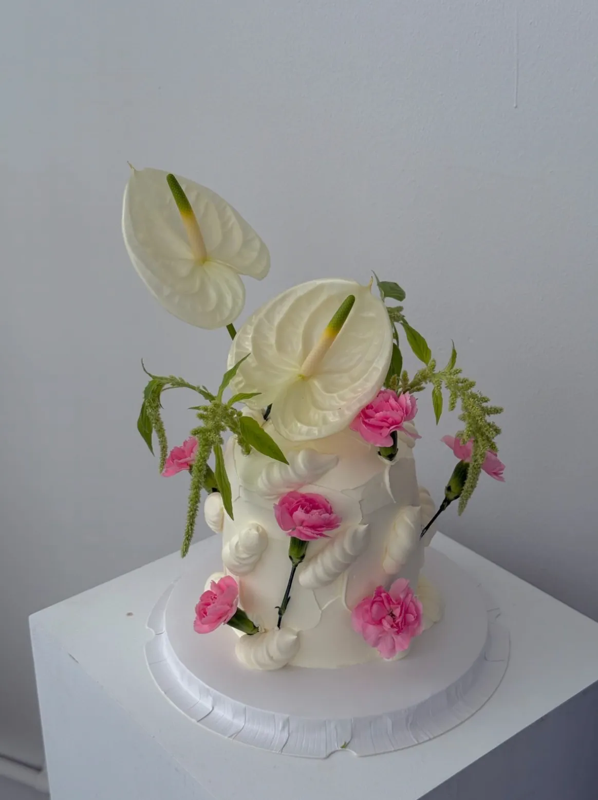 White textured buttercream cake topped with fresh white anthurium and pink carnations